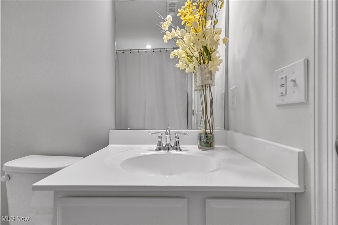Bathroom vanity with a white oval sink, chrome faucet, mirror, and tall arrangement of yellow and white flowers.