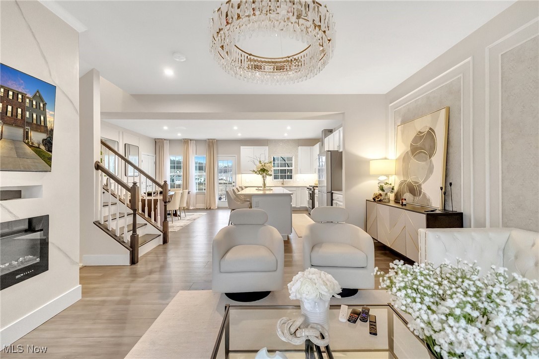 Open-plan living room with white lounge chairs, a glass coffee table, and kitchen island beyond.