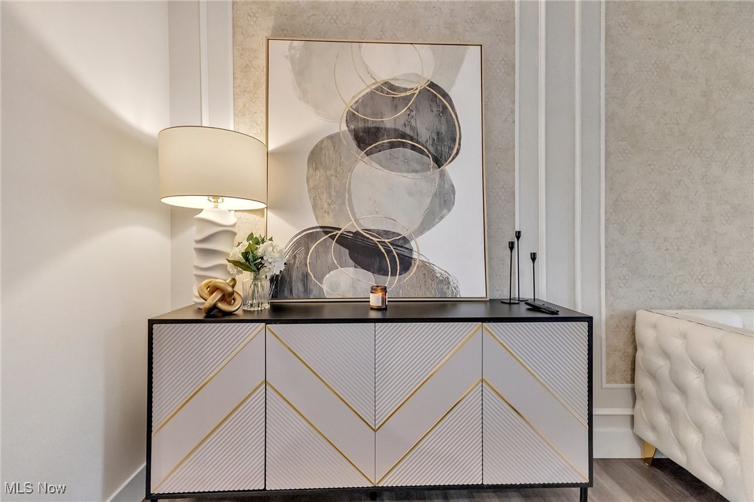 Geometric white-and-gold console cabinet beneath abstract artwork, beside a sculptural lamp and tufted chair.