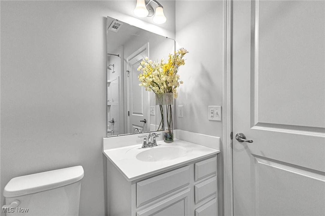 Bathroom with a white vanity, large mirror, and vase of yellow flowers.