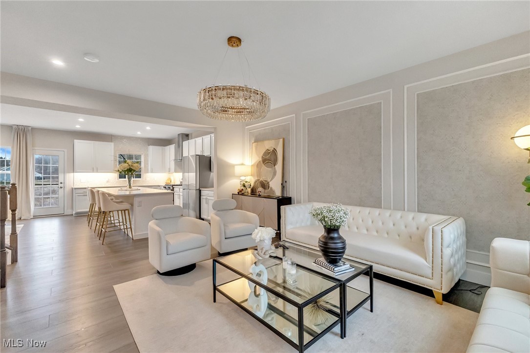 Staged living room with a white tufted sofa, glass coffee table, and open kitchen.