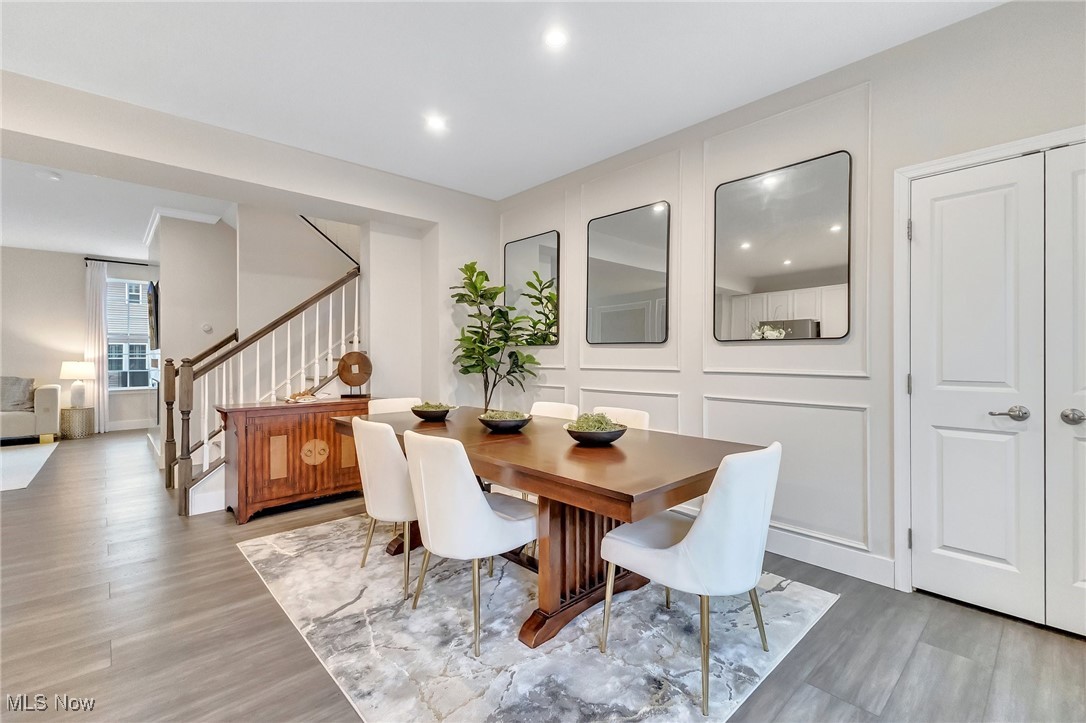 Dining room with a wooden table, white chairs, paneled walls, and a staircase.