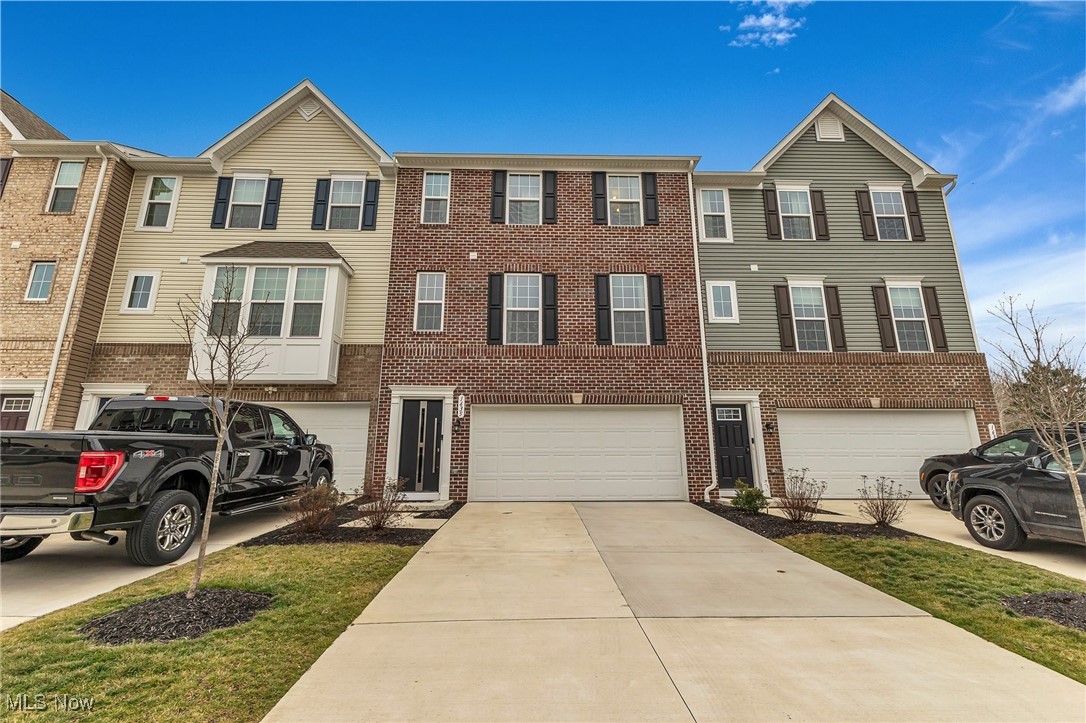 Townhouse exterior with brick and siding, attached garages, and a wide concrete driveway.