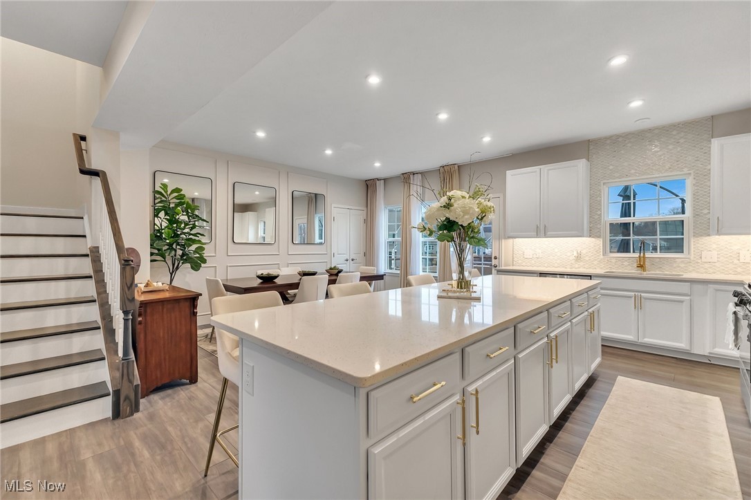 Bright white kitchen with a large island, brass fixtures, and an adjoining dining area beside a staircase.