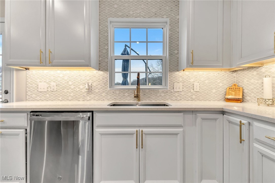 Kitchen with white cabinets, brass hardware, patterned tile backsplash, and sink beneath a window.