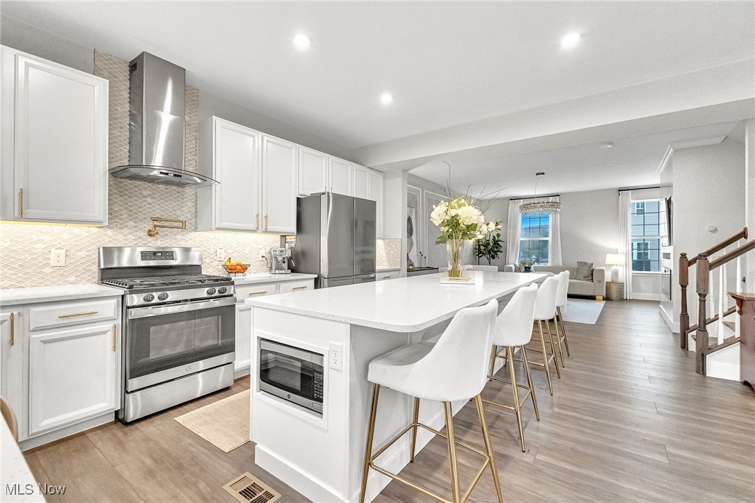 Bright kitchen with white cabinetry, stainless steel appliances, and a large island with white barstools.