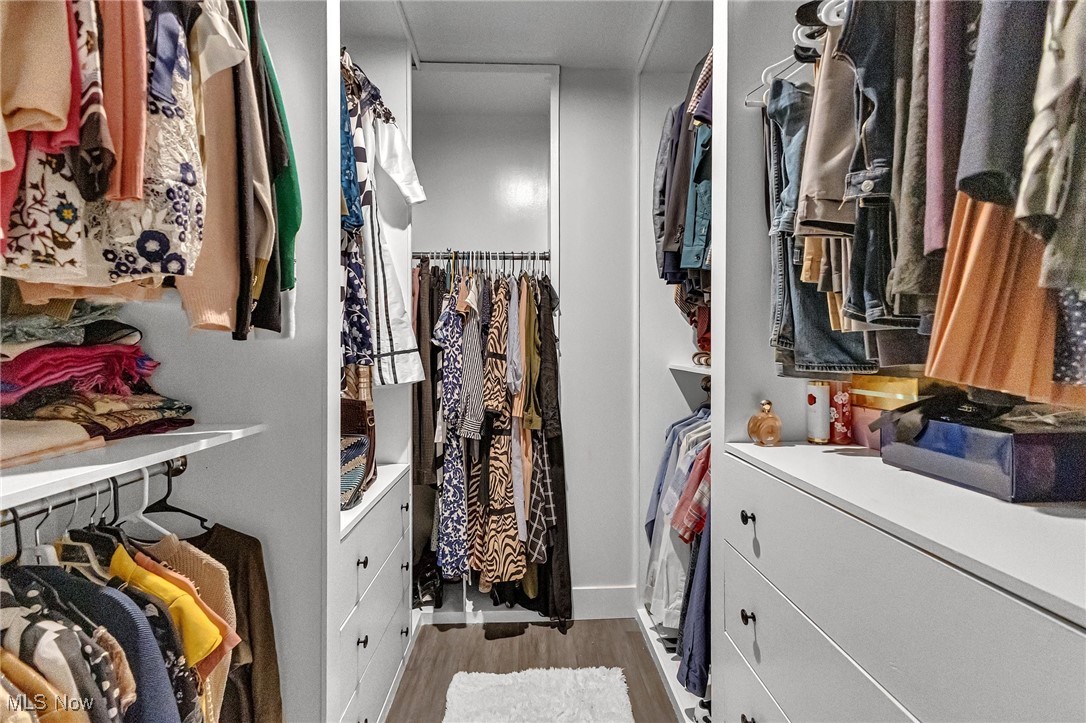 Walk-in closet with hanging clothes, built-in white drawers, and a white rug.