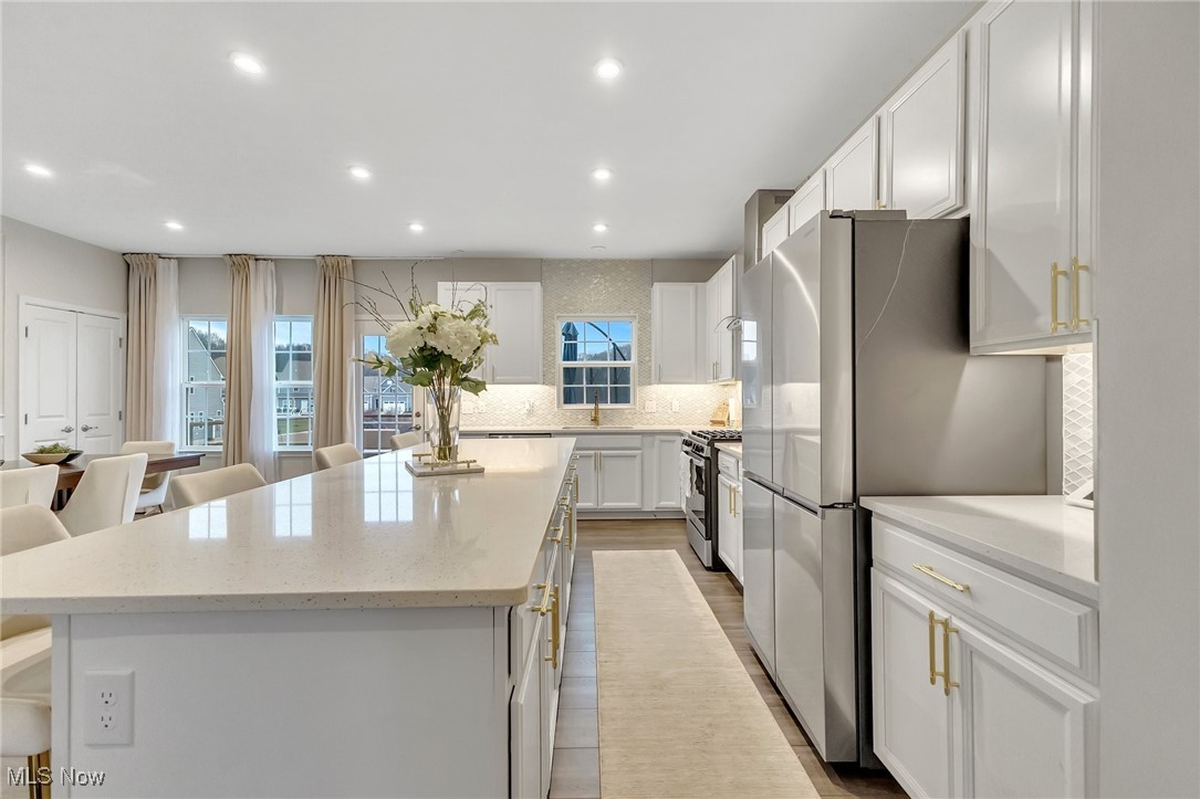 Bright white kitchen with a large quartz island, gold hardware, and stainless steel appliances.