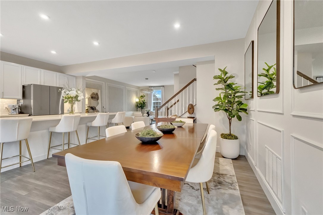 Dining room with a long wooden table beside an open kitchen and staircase.