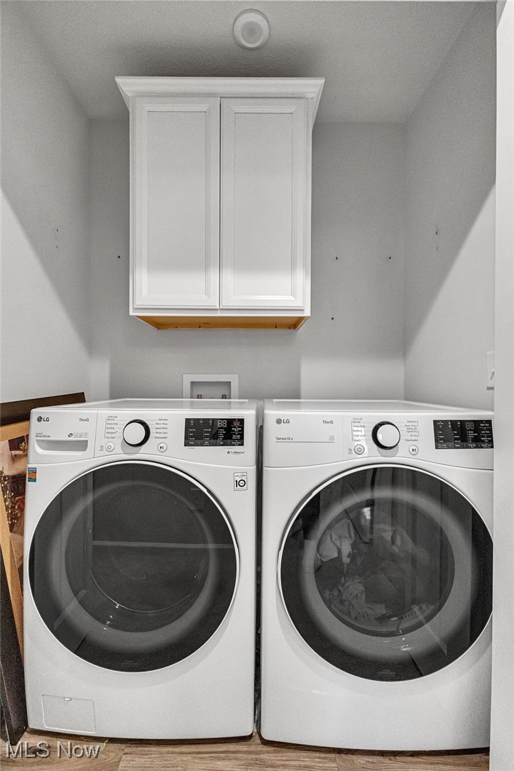 Laundry room with white front-loading washer and dryer beneath a wall cabinet.