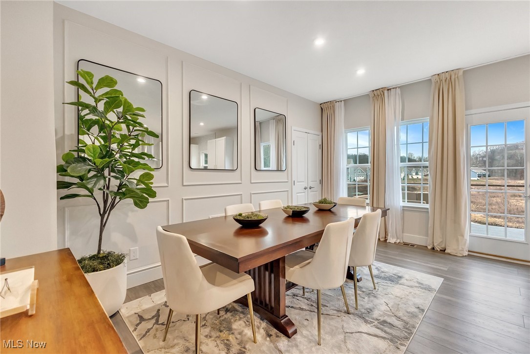 Dining room with a wood table, cream chairs, paneled walls, and tall curtained windows.