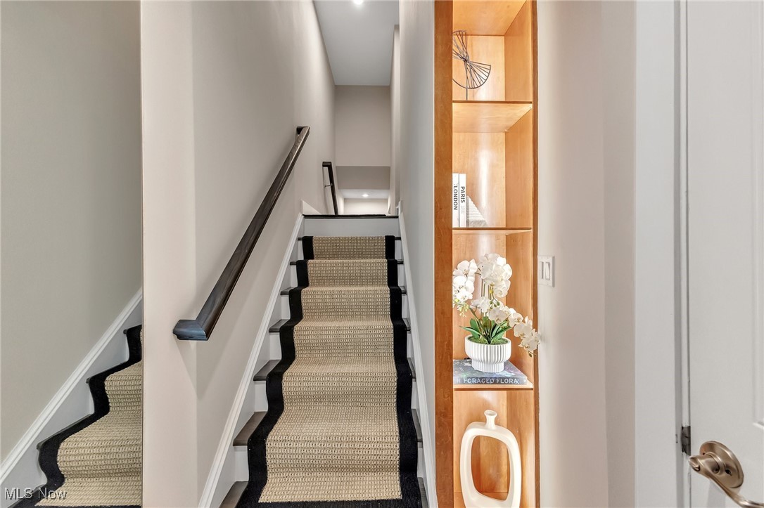 Carpeted staircase with a dark-edged runner beside a built-in wood display shelf and white orchid.