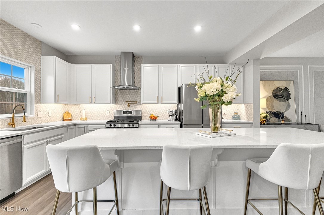 Bright white kitchen with a large quartz island, gold-tone fixtures, and stainless steel appliances.