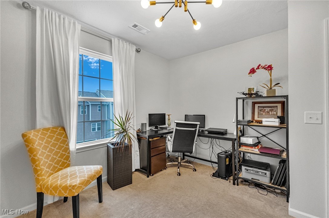 Home office with dual monitors, open shelving, and a yellow patterned chair beside a tall window.