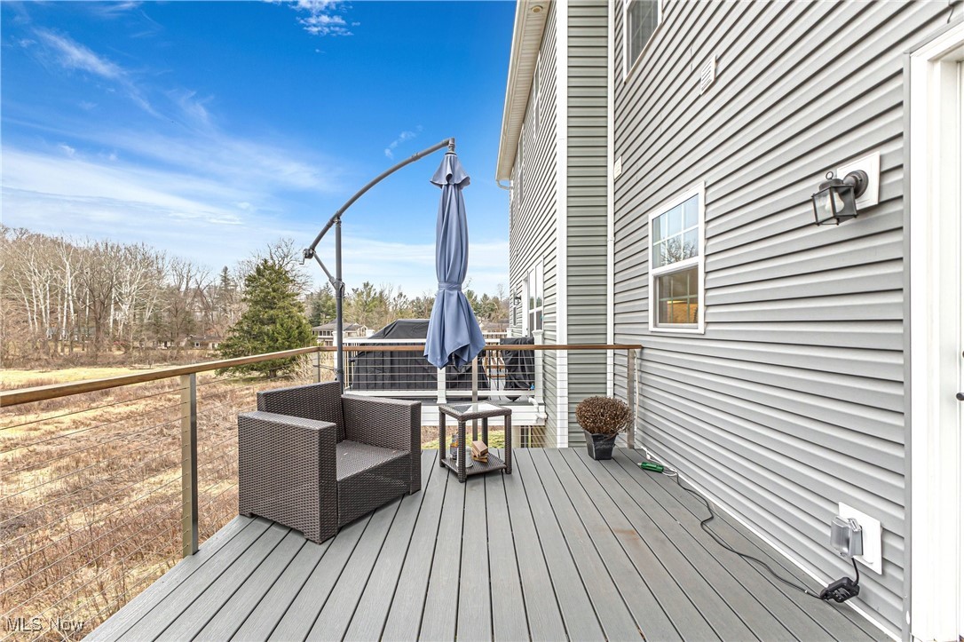 House deck with wicker chairs and closed umbrella overlooking leafless trees.