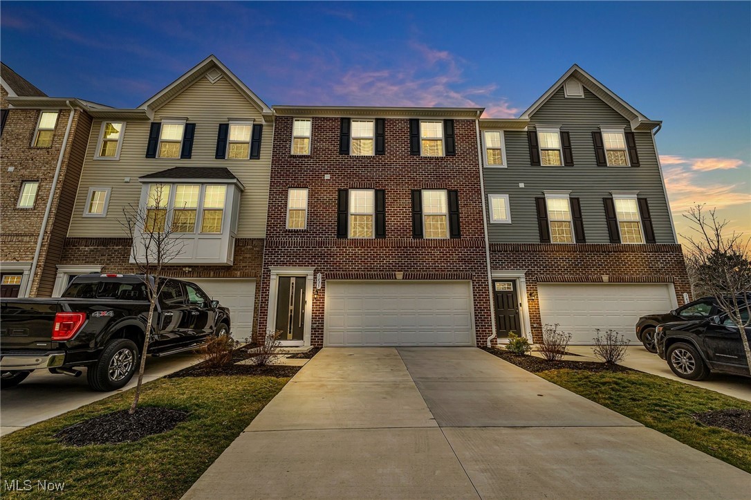 Attached townhomes with brick facades, multiple garages, and a broad concrete driveway at dusk.