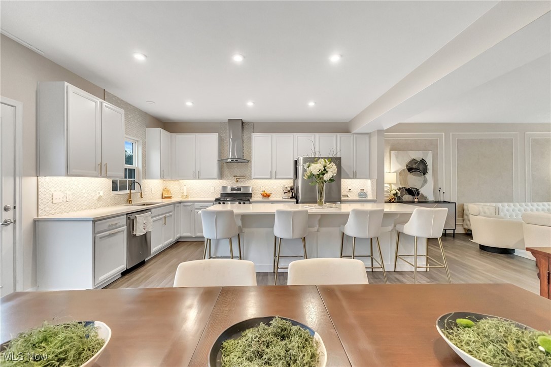 Open kitchen with white cabinets, stainless steel appliances, and a large island with four bar stools.