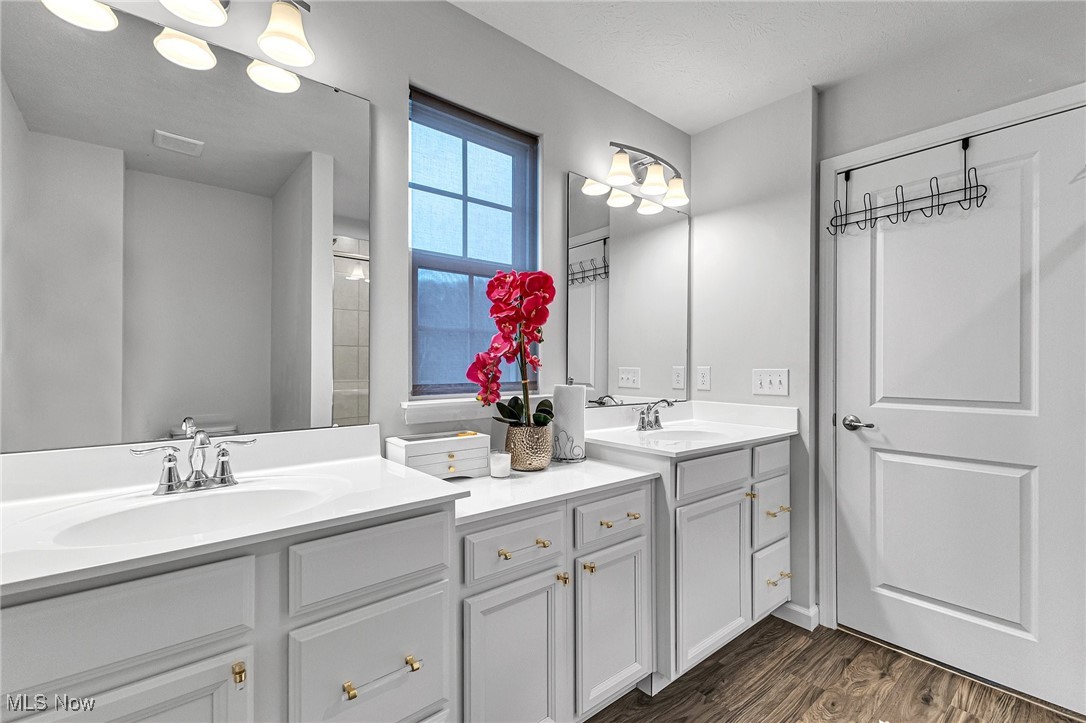 Bathroom with two white vanities, large mirrors, a window, and a pink orchid between the sinks.