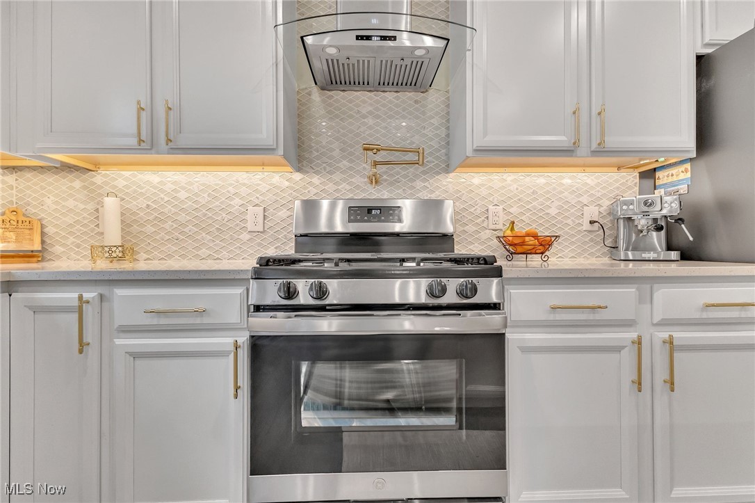 Kitchen with white cabinets, gold hardware, stainless steel range, and diamond-pattern tile backsplash.