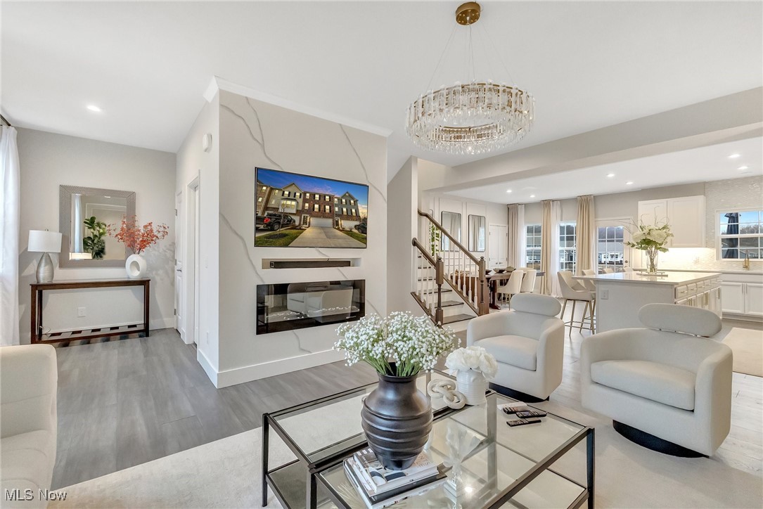 Staged living room with a marble-look fireplace, crystal chandelier, and open kitchen and dining area.