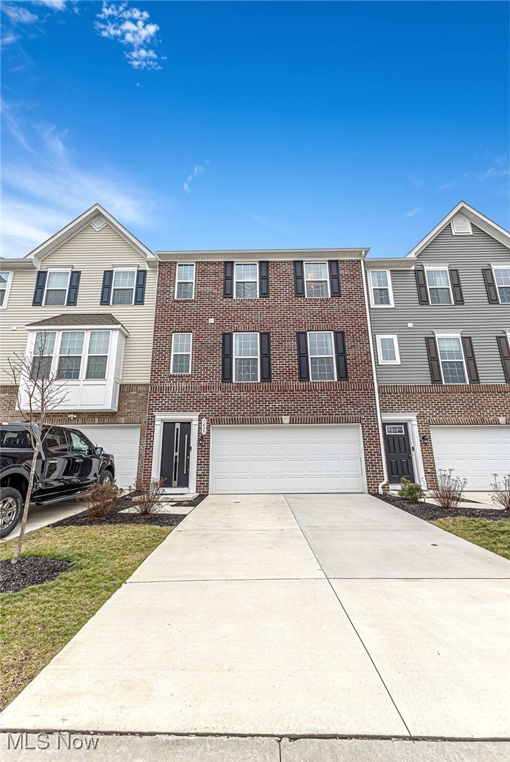 Three-story brick-and-siding townhome with black shutters and a wide concrete driveway.