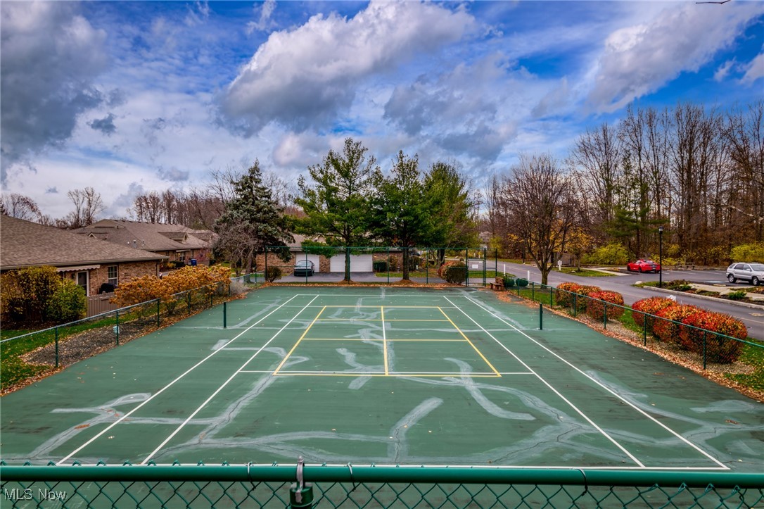 Fenced tennis court with a worn green surface, surrounded by autumn trees.