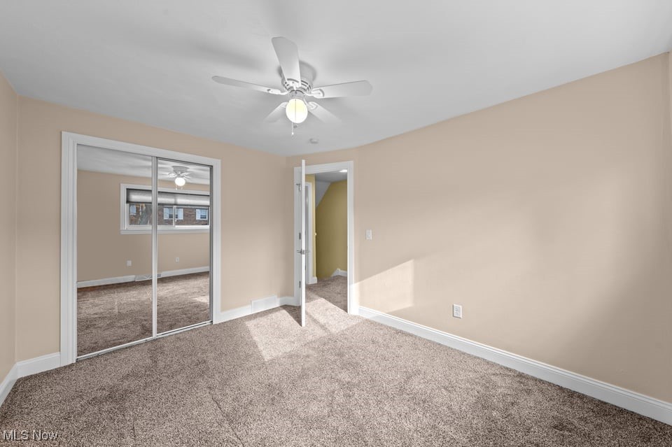 Empty carpeted bedroom with mirrored closet doors, a ceiling fan, and sunlight by the open doorway.
