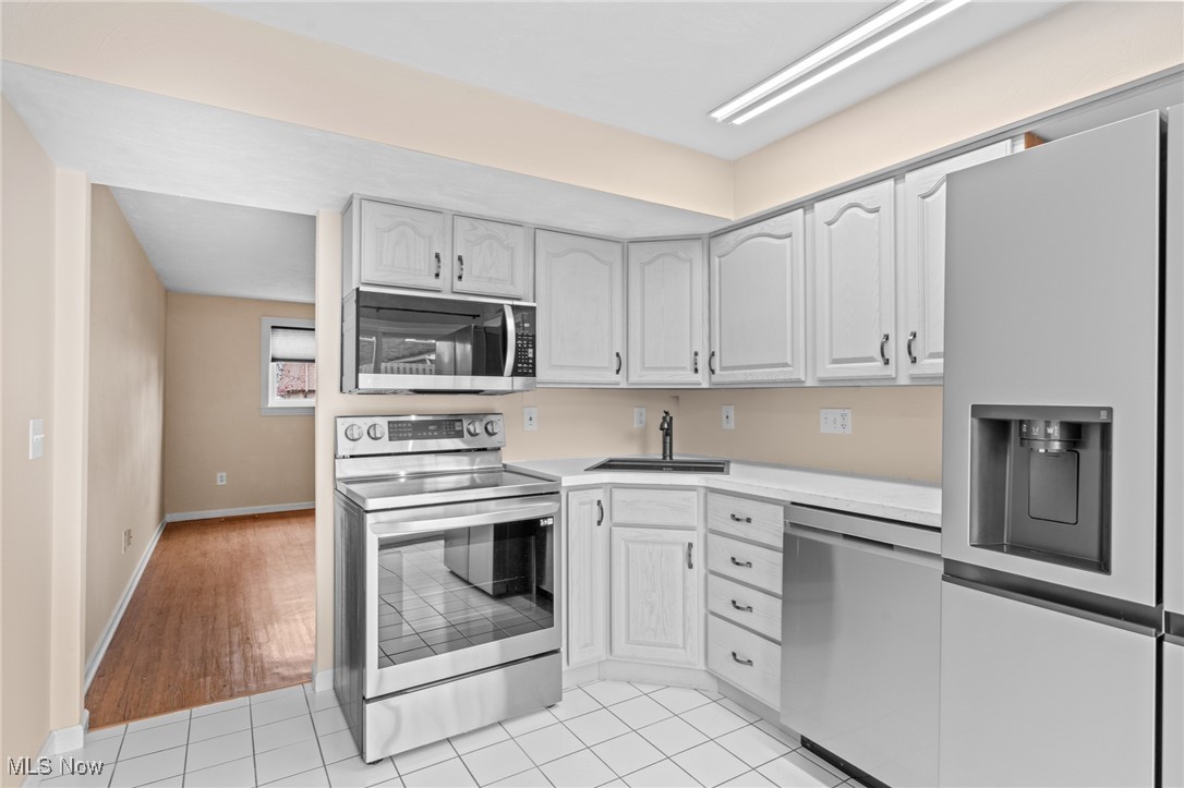 Kitchen with white cabinets, stainless steel appliances, and white tile flooring.