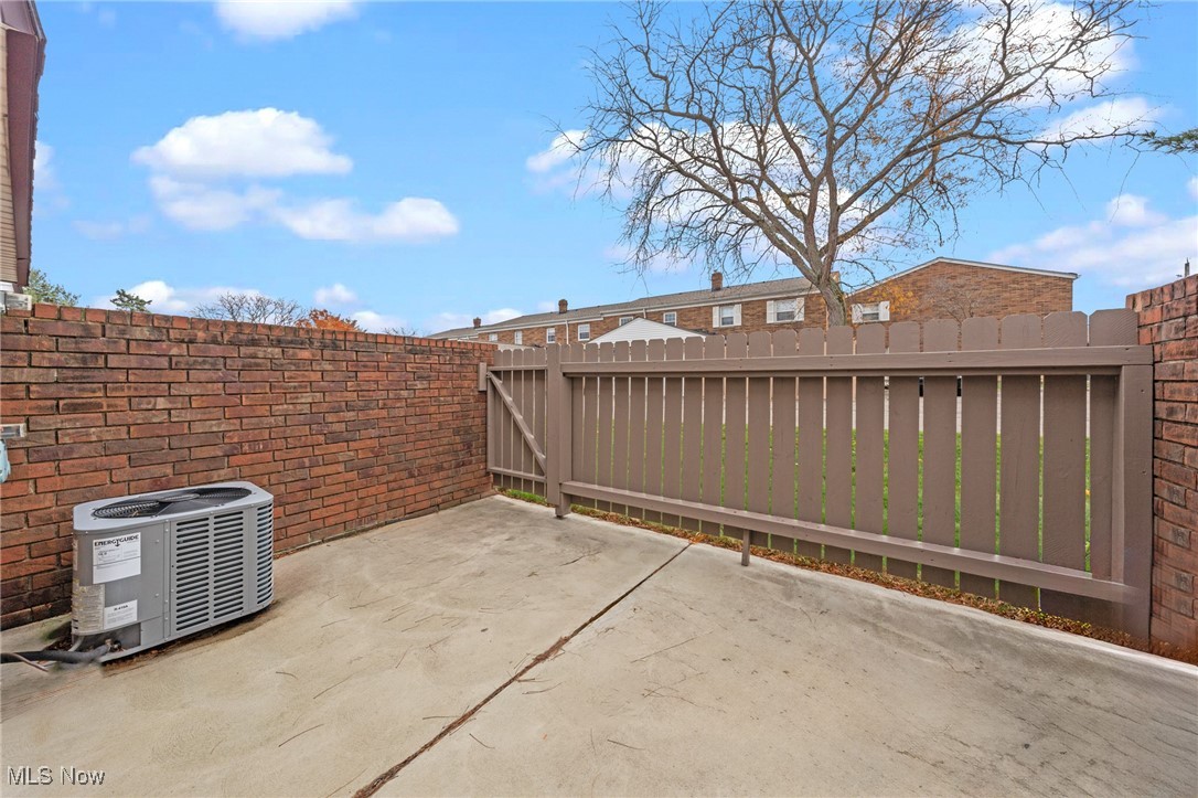 Paved patio enclosed by brick walls and a privacy fence, with an air-conditioning unit at the left.