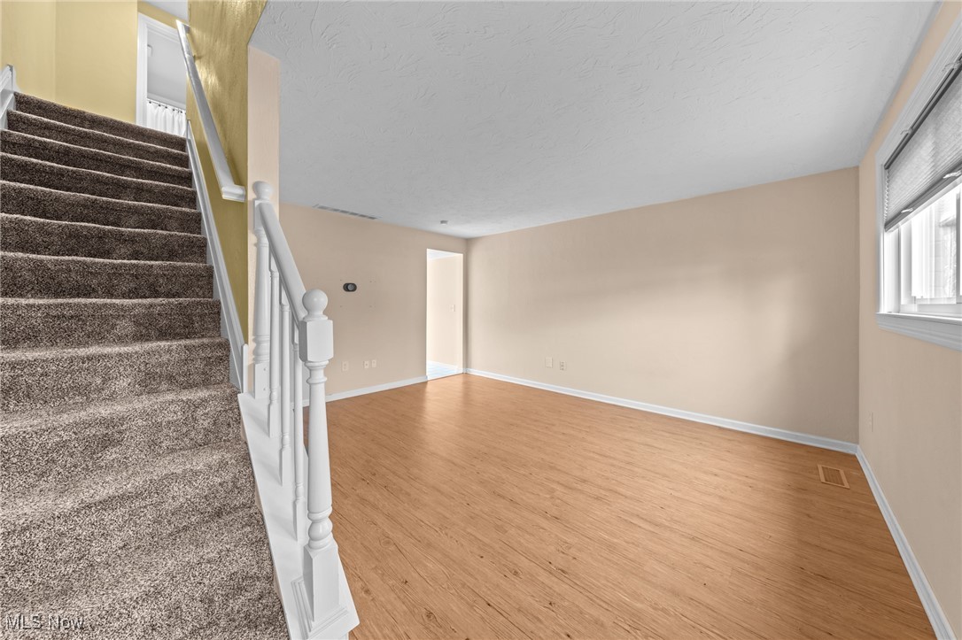 Empty living room with wood flooring beside a carpeted staircase and white railing.