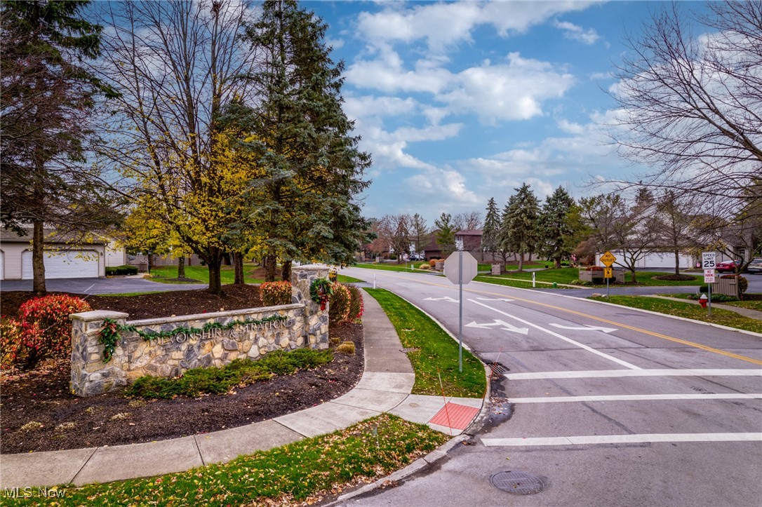 Neighborhood entrance with a stone community sign beside a tree-lined residential intersection.