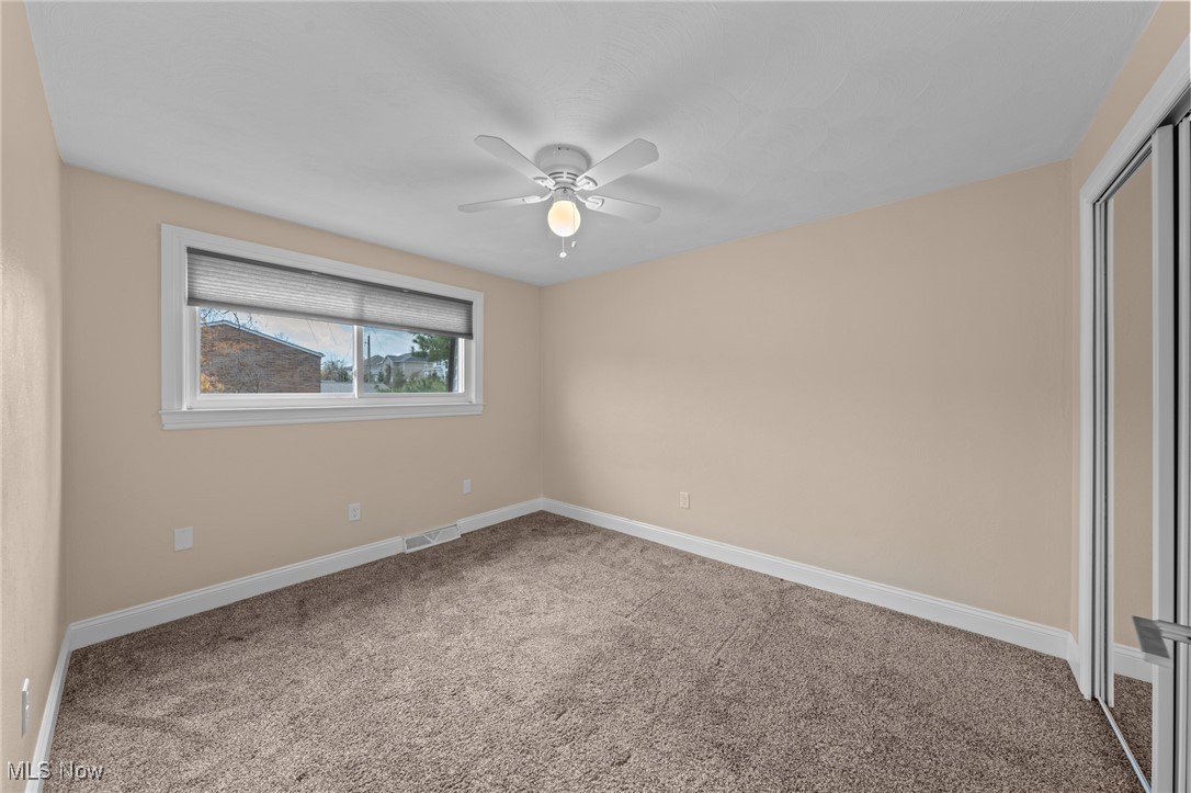Empty bedroom with brown carpet, a ceiling fan, and mirrored sliding closet doors.