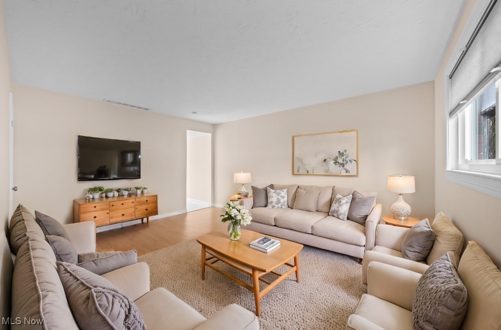 Furnished living room with cream seating, a wooden coffee table, and a television above a chest.