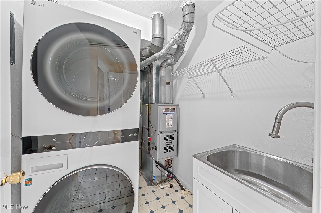 Laundry room with stacked washer and dryer, utility sink, and wall-mounted drying racks.