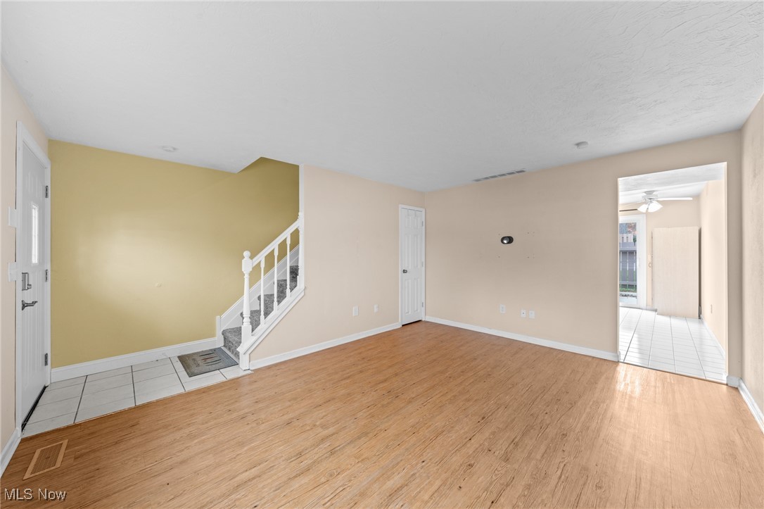 Empty living room with wood floors, tiled entry, and a carpeted staircase.