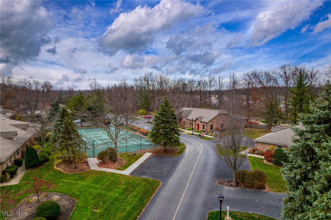 Aerial view of brick homes and a tennis court beside a curving neighborhood street.