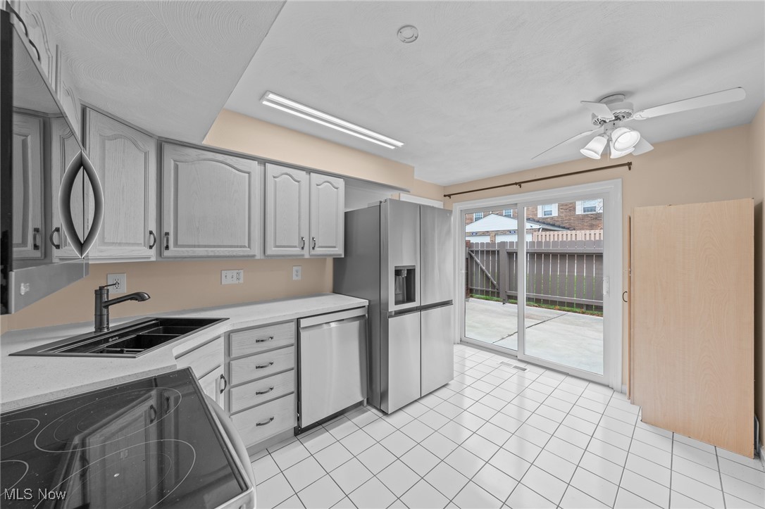 Kitchen with white tile floors, gray cabinets, stainless steel appliances, and sliding patio doors.