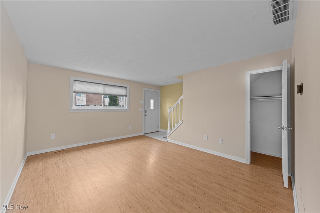 Empty living room with light wood floors, a front door, staircase, and open closet.