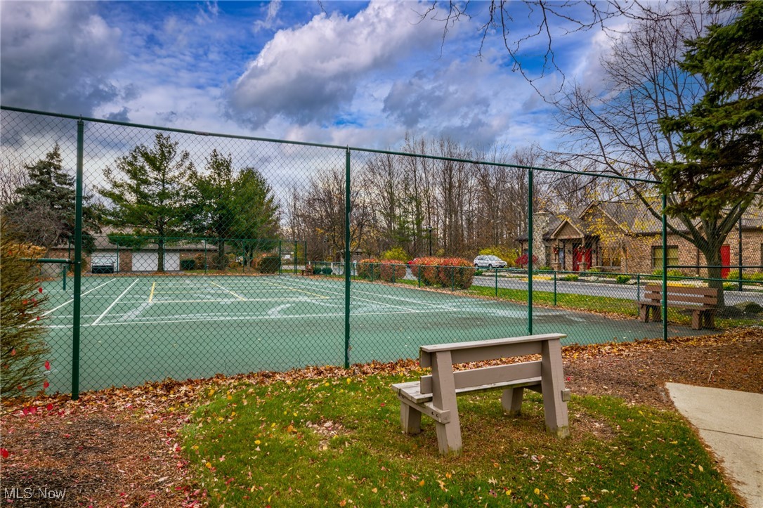 Fenced outdoor tennis court with painted lines and benches beside homes.