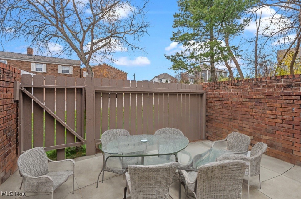 Enclosed patio with a glass table, woven chairs, wooden gate, and brick walls.