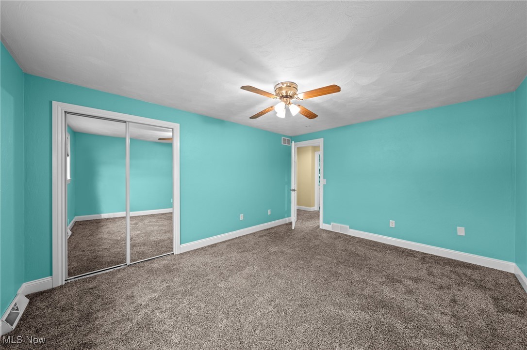 Vacant bedroom with turquoise walls, mirrored closet doors, gray carpet, and a ceiling fan.