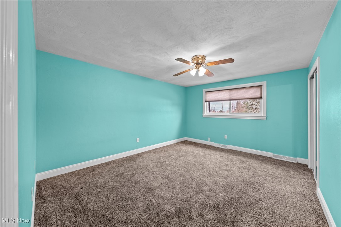 Empty bedroom with turquoise walls, beige carpet, a small shaded window, and a ceiling fan.