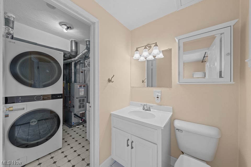 Bathroom with white vanity and toilet, opening to a laundry area with stacked washer and dryer.