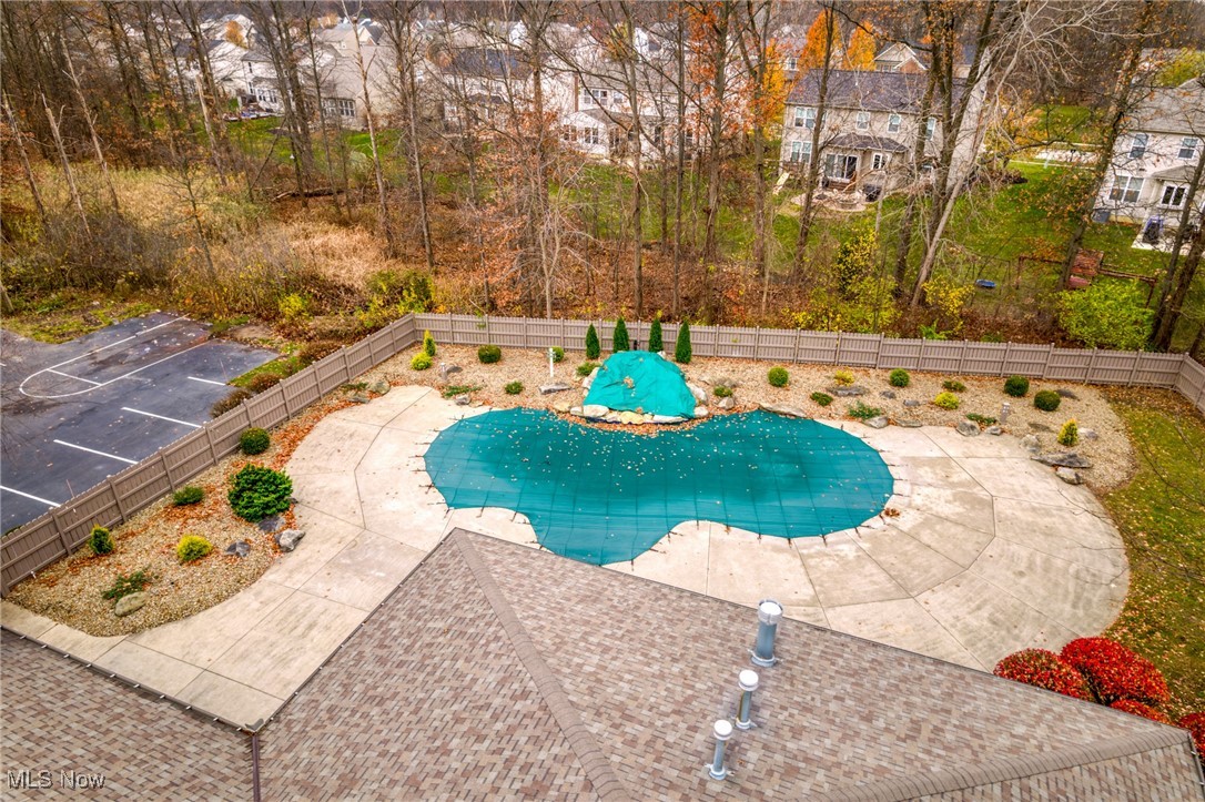 Aerial view of a covered backyard pool, broad patio, fenced yard, and nearby basketball court.