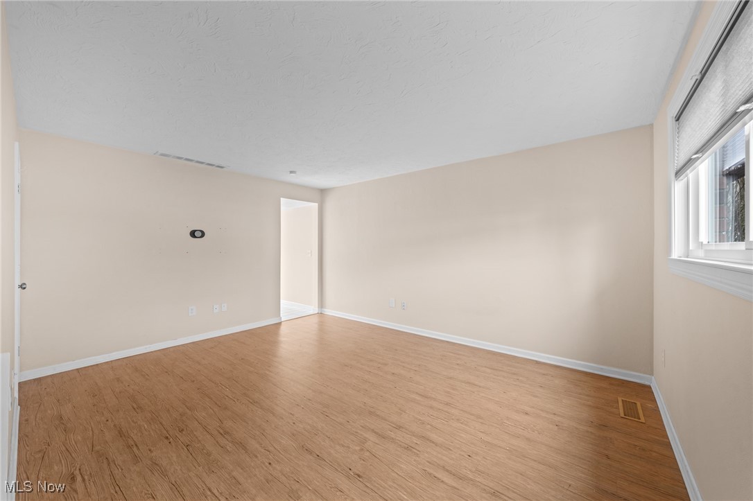 Vacant room with wood flooring, beige walls, and a large window.
