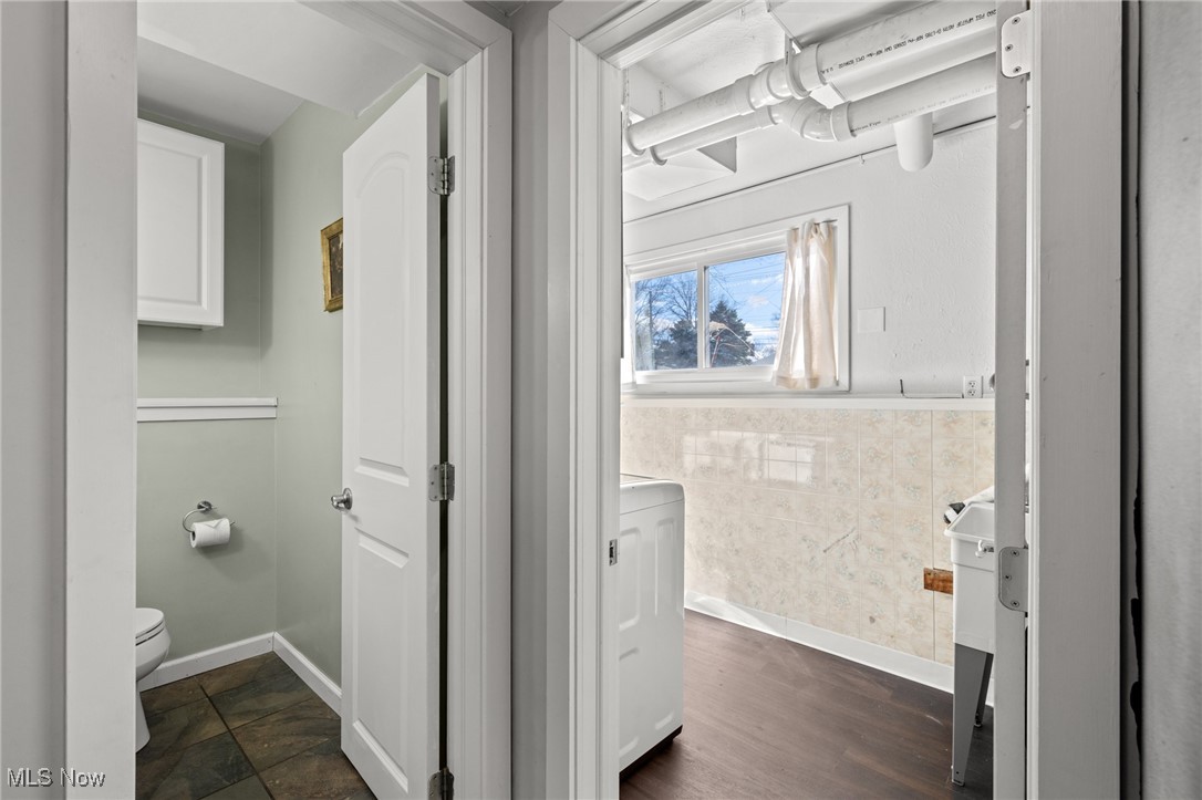 Laundry room with exposed ceiling ductwork beside a small half bathroom.