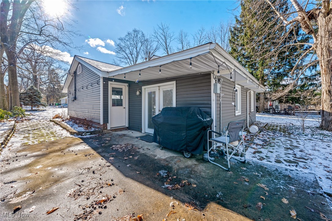 Gray-sided home with a broad covered patio, grill, and outdoor chairs in a snowy yard.