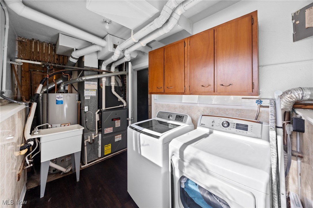 Laundry room with washer, dryer, utility sink, and wooden cabinets.