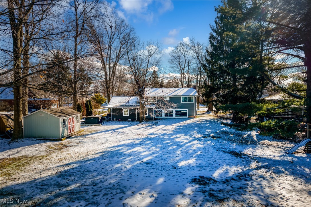 Blue split-level home with a snowy backyard, small shed, and tall evergreen.