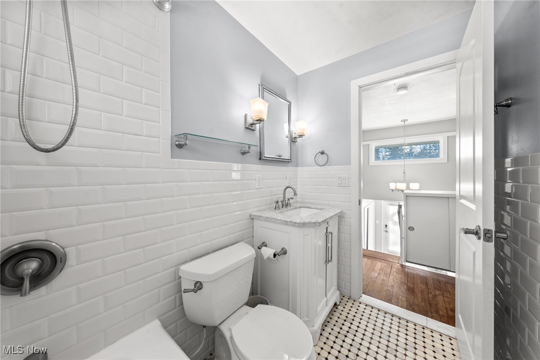 Bathroom with white subway tile, mosaic floor, and a vanity beside an open doorway.